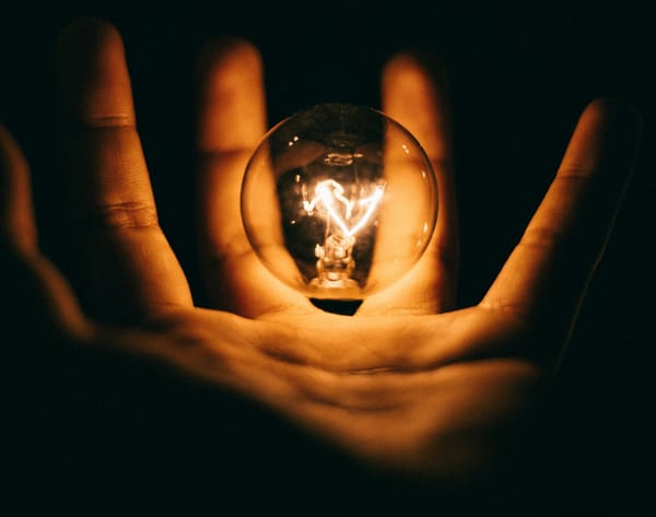 A hand holding a light bulb in the dark